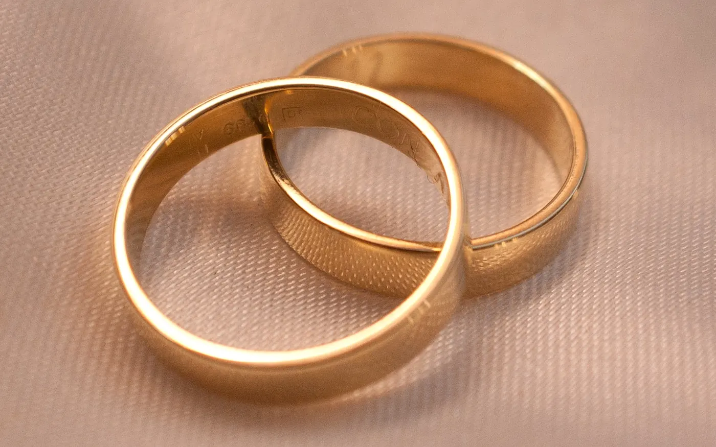 Dos alianzas de boda entrelazadas sobre una tela de color crema