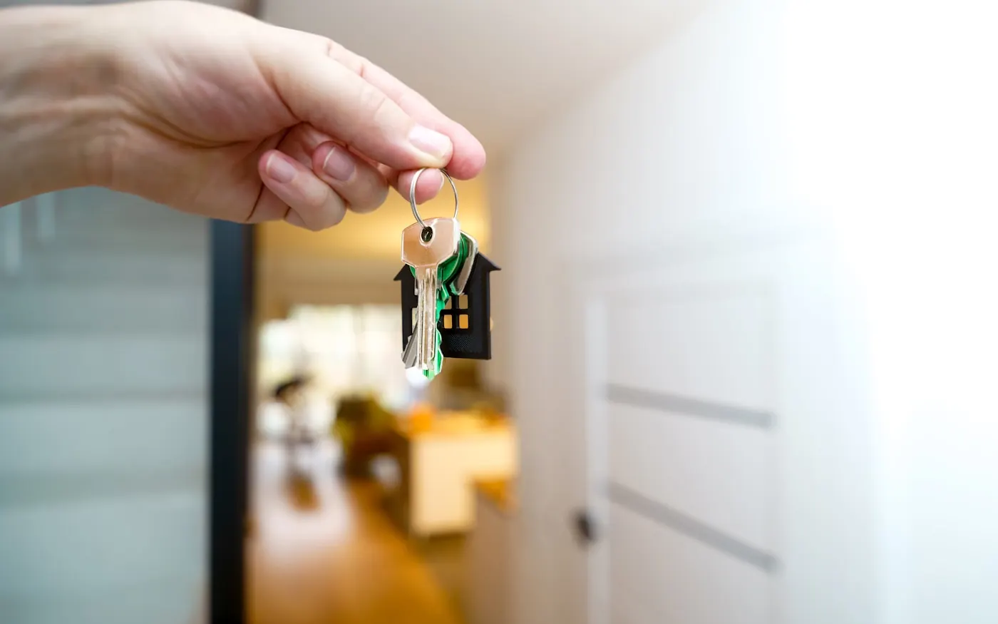Manos sosteniendo las llaves de una vivienda ante la puerta de entrada