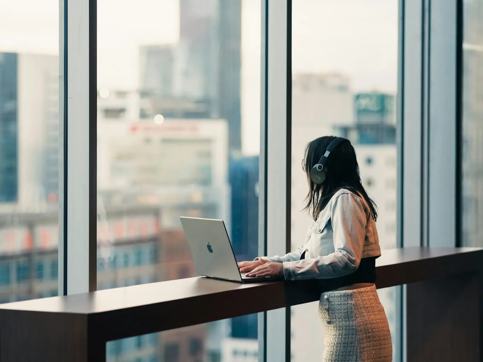 Empresaria siguiendo una clase online con auriculares junto a la ventana